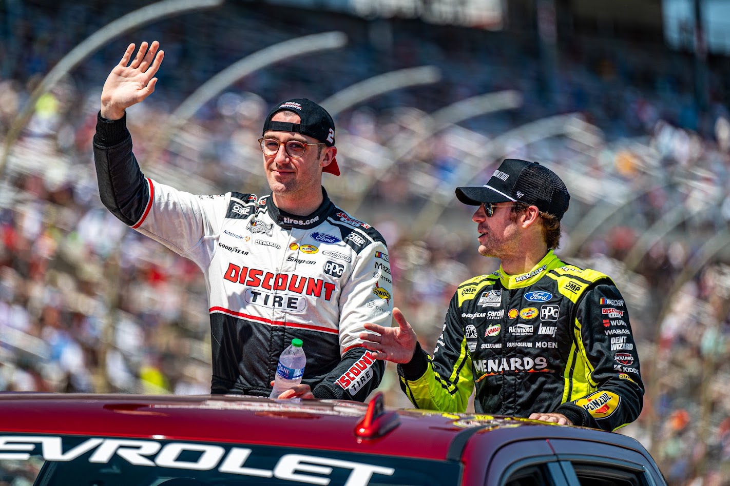 Austin Cindric waving and Ryan Blaney beside him in their Team Penske fire suits during driver introductions