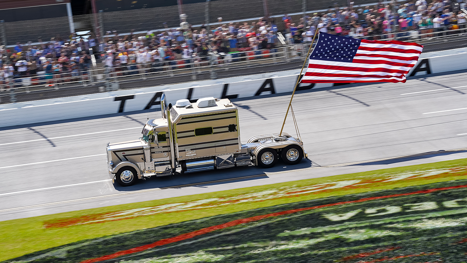 A truck carrying an American flag runs down the frontstretch at Talladega in front of the grandstand